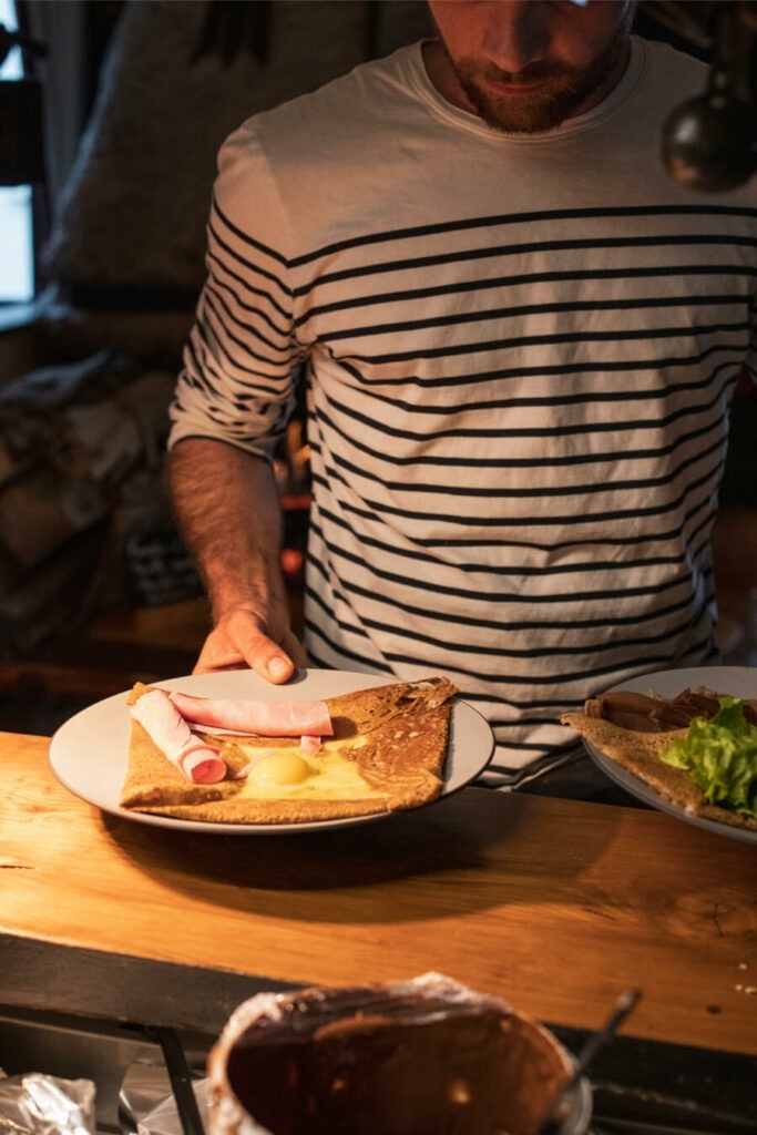 Homme présentant une assiette avec une crêpe au jambon